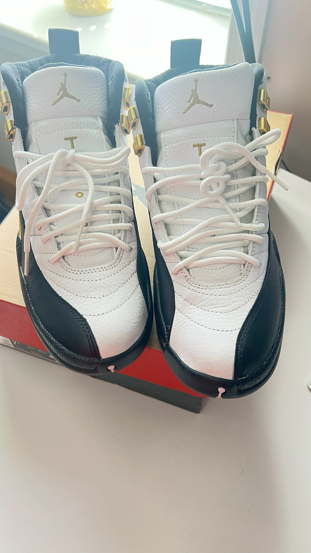 Shop Nova Finds Air Jordan 12 Retro high-top sneakers in white leather with black overlays and gold hardware accents.